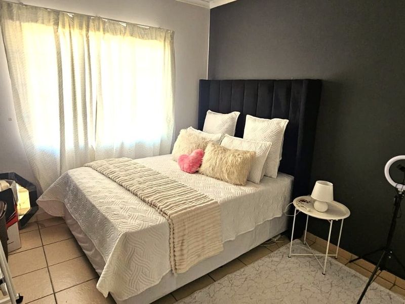 A well-maintained bedroom featuring tiled flooring, a dark accent wall, and natural light through window curtains.