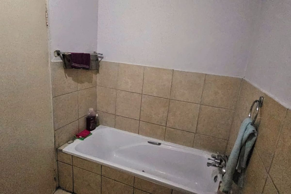 A functional bathroom featuring a built-in bathtub with tiled surround and wall-mounted towel rails.