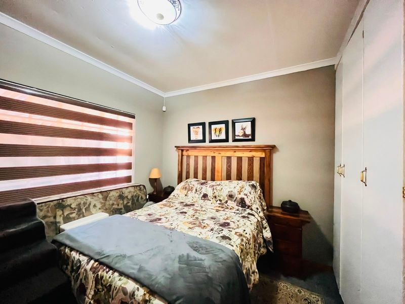 A functional bedroom featuring built-in cupboards, ceiling cornice detailing, and fitted roller blinds, providing a neutral base for personalization.