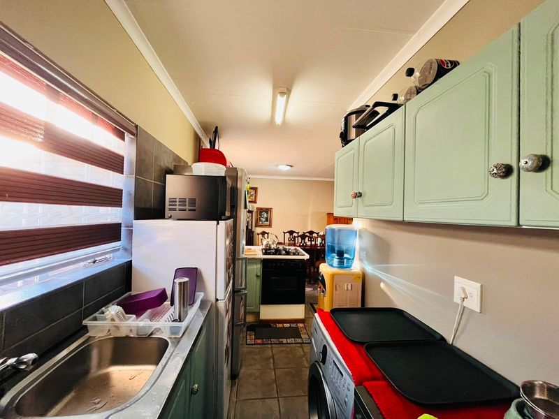 A functional scullery area featuring built-in cabinetry, a stainless steel sink, tiled splashbacks, and direct access to the kitchen and dining space.