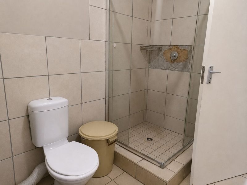 A bathroom featuring a toilet and a shower enclosure with visible damage to the wall tiling around the shower mixer.