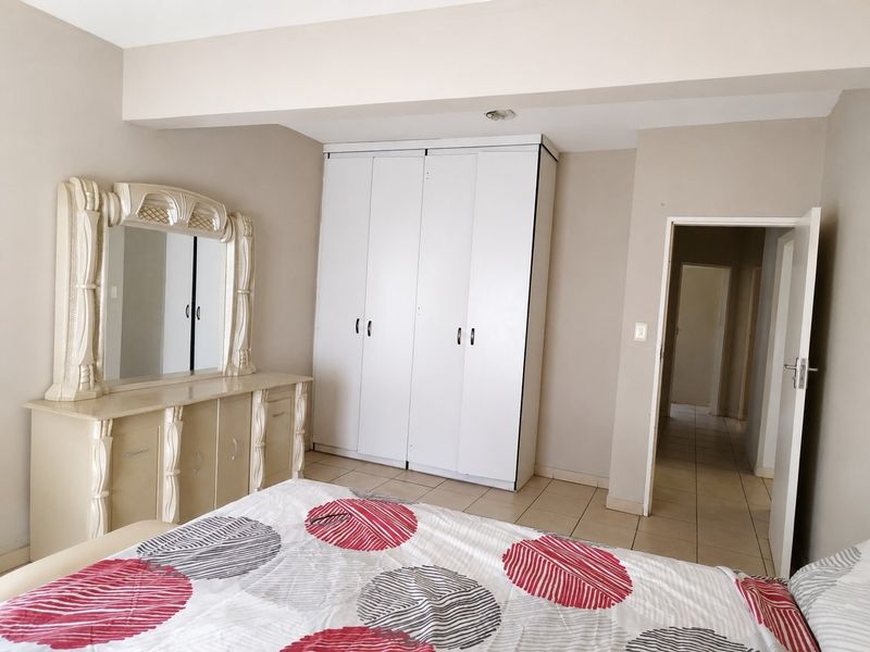 A bedroom featuring neutral wall tones, tiled flooring, and a white built-in wardrobe providing ample storage space.