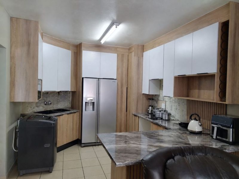 Modern kitchen featuring wood-grain and white cabinetry, stone-look countertops, and a double basin sink, currently awaiting backsplash installation.