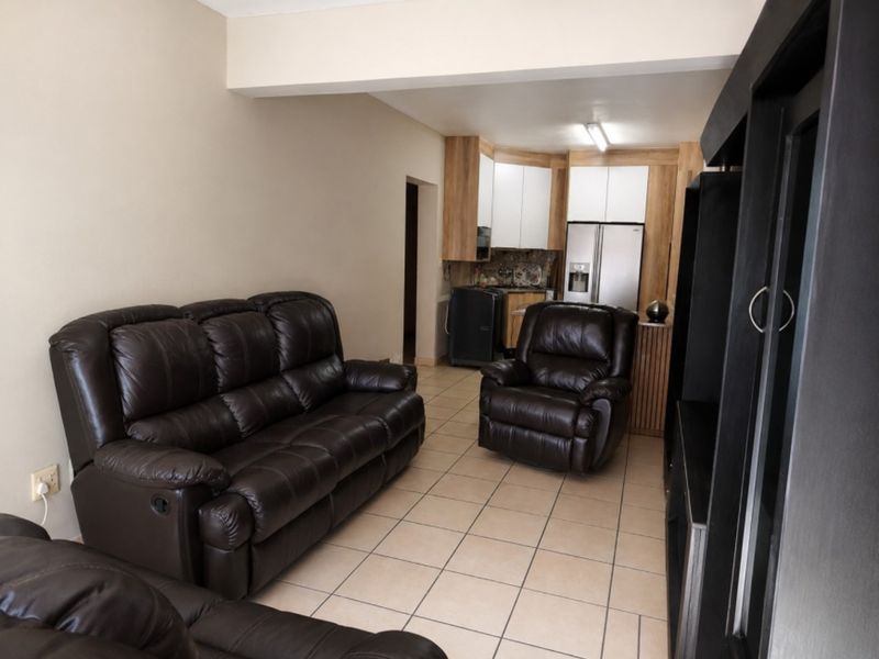 Open-plan living area featuring tiled flooring and a functional kitchen with built-in cabinetry, seamlessly connecting the lounge and kitchen spaces.