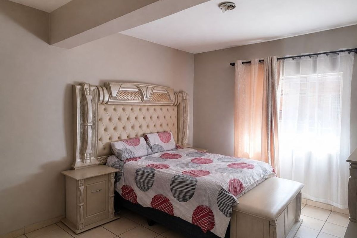 A bedroom featuring tiled flooring, a ceiling bulkhead, and a window fitted with security bars.