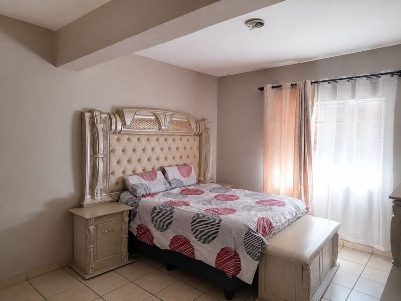 A bedroom featuring tiled flooring, a ceiling bulkhead, and a window fitted with security bars.