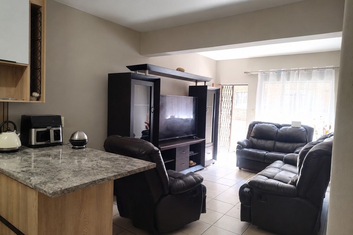 Open-plan living area featuring a kitchen breakfast bar with stone-look countertop, ceramic tiled flooring, and direct access to the exterior through a security gate.