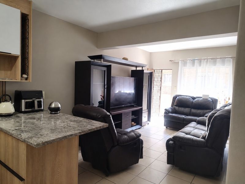 Open-plan living area featuring a kitchen breakfast bar with stone-look countertop, ceramic tiled flooring, and direct access to the exterior through a security gate.