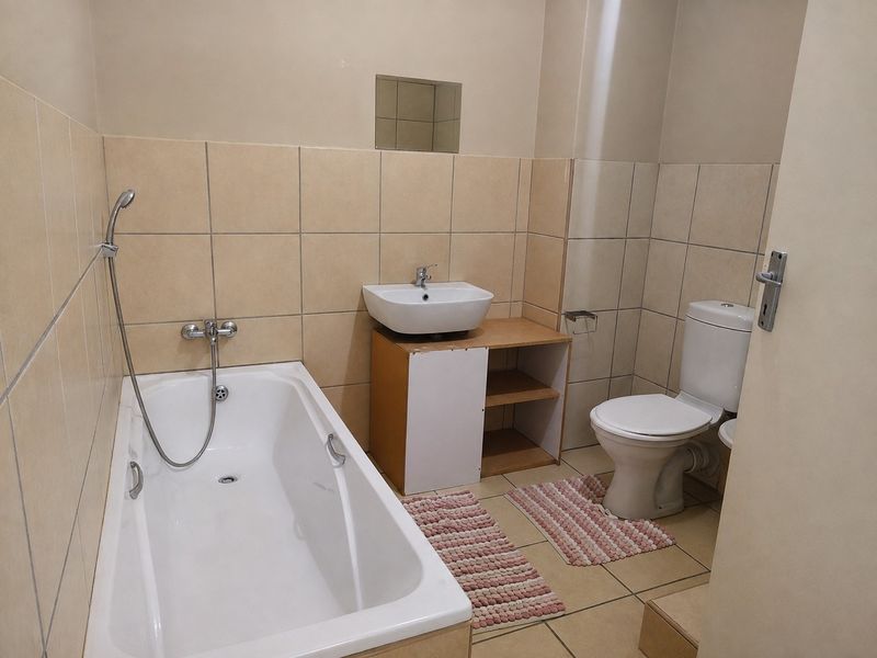 A functional bathroom featuring a bathtub with handheld shower, a basin with vanity cabinet, and a standard toilet with tiled finishes.