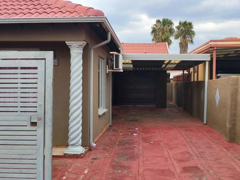 Front exterior view featuring a gated driveway, carport, garage access, and perimeter walling with decorative architectural elements.