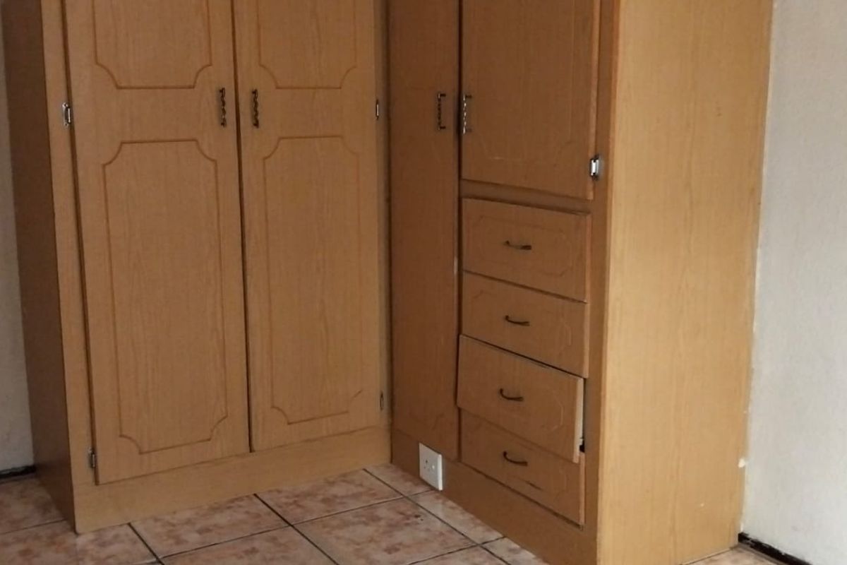 A bedroom featuring built-in wooden cupboards and tiled flooring, showing signs of wear and requiring minor maintenance.