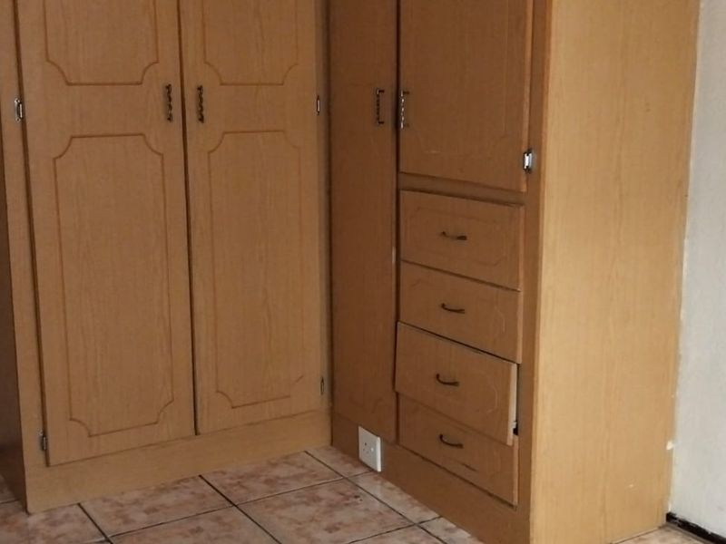 A bedroom featuring built-in wooden cupboards and tiled flooring, showing signs of wear and requiring minor maintenance.