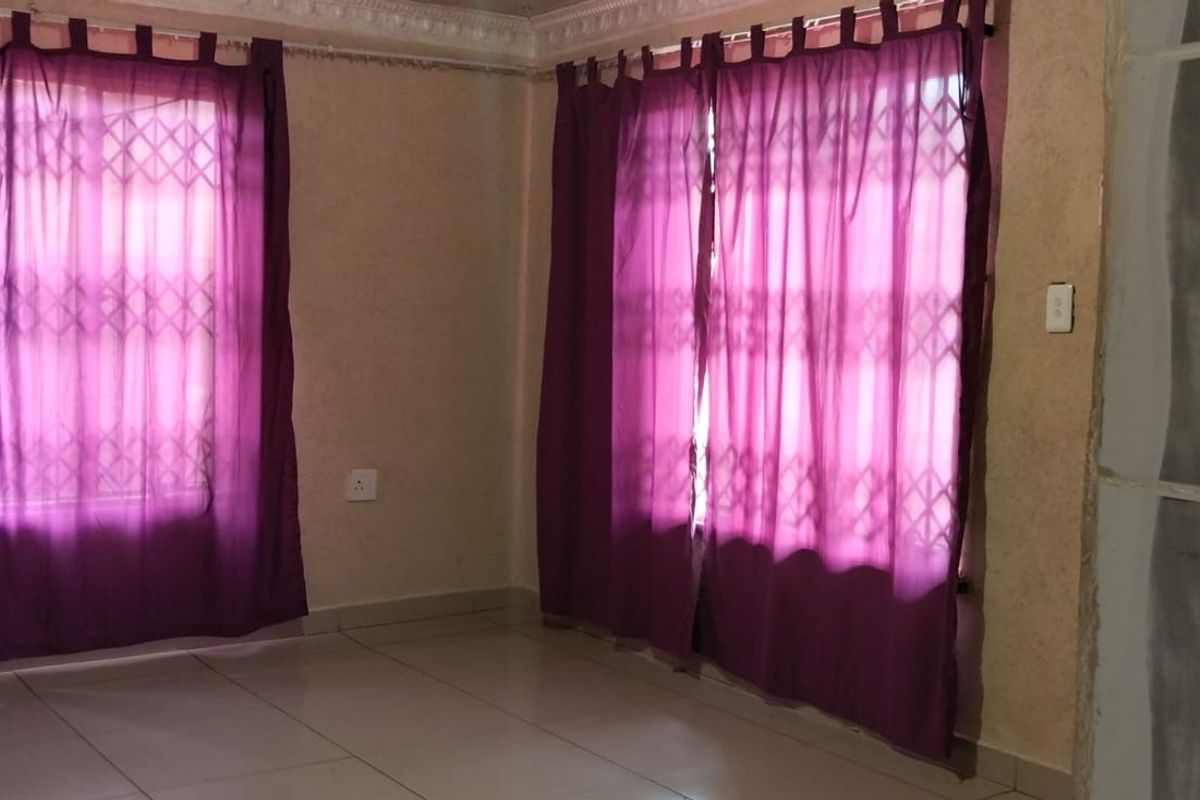 An empty living area featuring tiled flooring, decorative cornicing, and security gates on the windows.