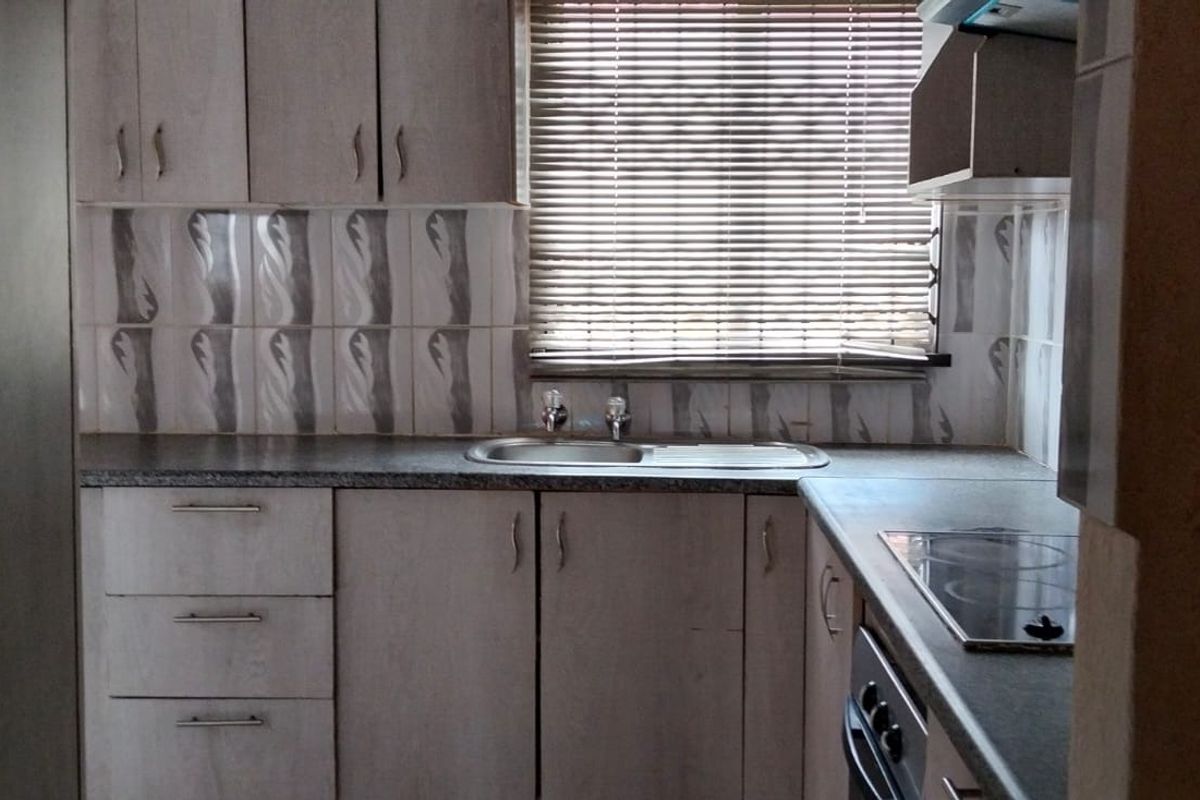 A functional kitchen featuring laminate cabinetry, tiled backsplash, built-in electric hob, oven, and a stainless steel sink with natural light from the window.