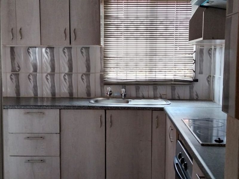 A functional kitchen featuring laminate cabinetry, tiled backsplash, built-in electric hob, oven, and a stainless steel sink with natural light from the window.