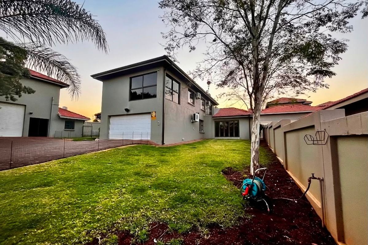 Rear view of a two-story residential property featuring a lawn, boundary wall, and integrated garage.