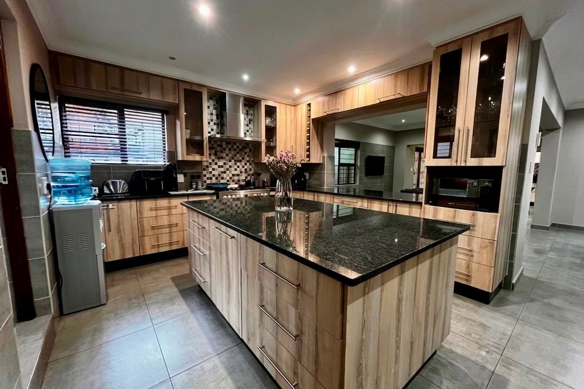 Modern kitchen featuring wood-finish cabinetry, a large granite-topped central island, mosaic backsplash, and integrated appliances with recessed lighting.
