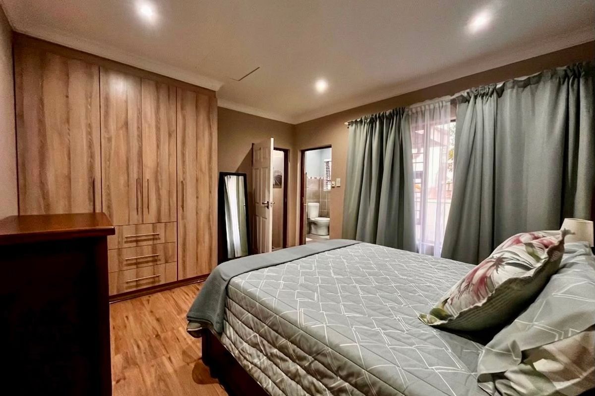 A well-maintained bedroom featuring wood-look laminate flooring, ample built-in cupboard storage, recessed lighting, and direct access to an en-suite bathroom.