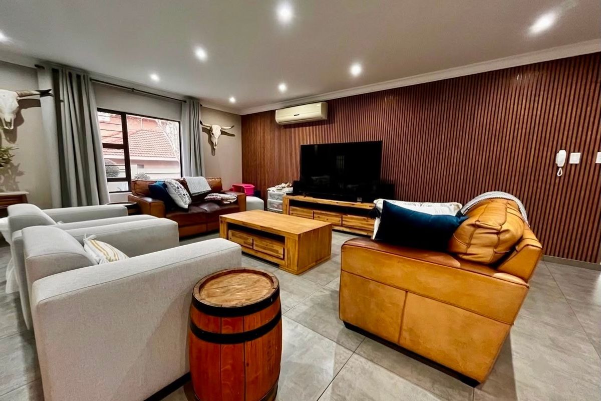 Spacious living room featuring modern slatted timber wall paneling, tiled flooring, recessed downlighting, and a wall-mounted split-system air conditioner.