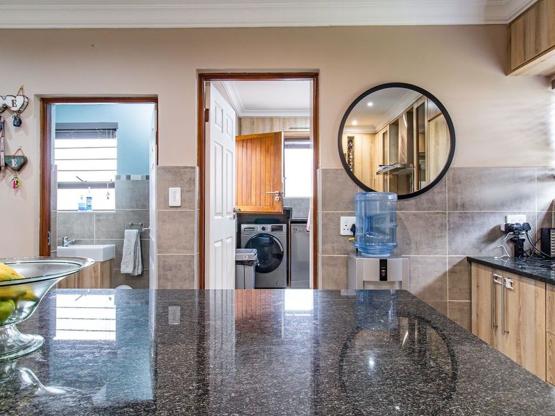 A well-maintained kitchen featuring granite countertops, modern cabinetry, and a tiled backsplash, with a clear view into the adjacent laundry and bathroom areas.