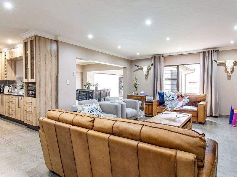 Spacious open-plan living area featuring a modern kitchen with wood-finish cabinetry, granite countertops, tiled floors, and seamless flow to the outdoor patio area.