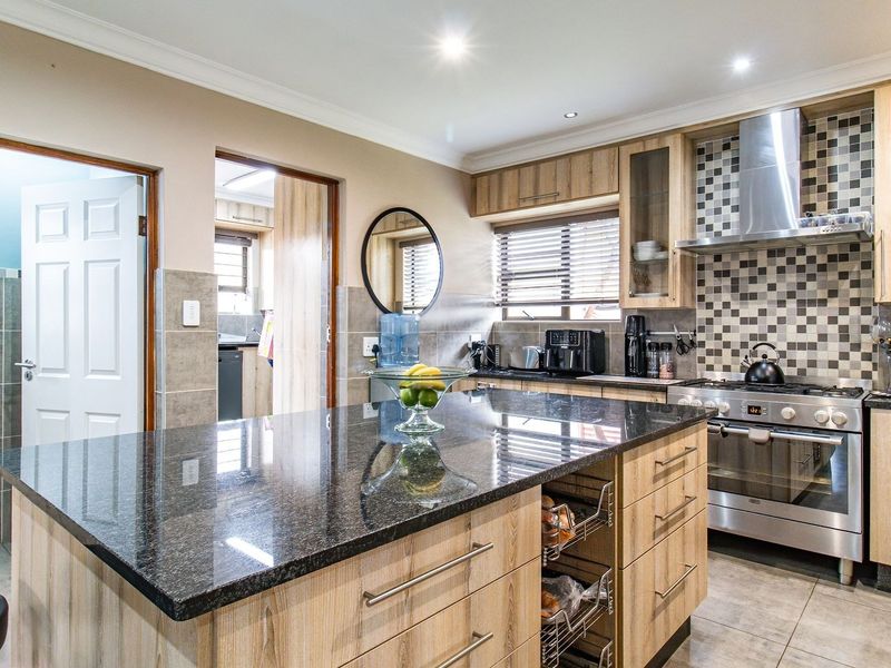 Modern kitchen featuring a large granite-topped island, stainless steel gas stove with extractor, and ample wooden cabinetry with a stylish mosaic tile backsplash.