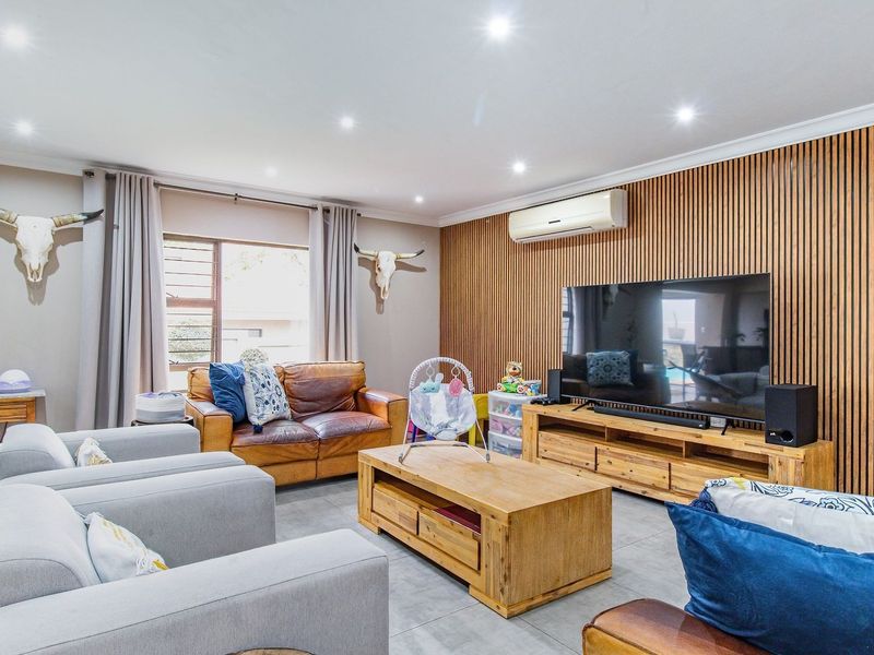 Spacious living room featuring a modern timber slat feature wall, recessed downlighting, tiled flooring, and a wall-mounted split-system air conditioner.