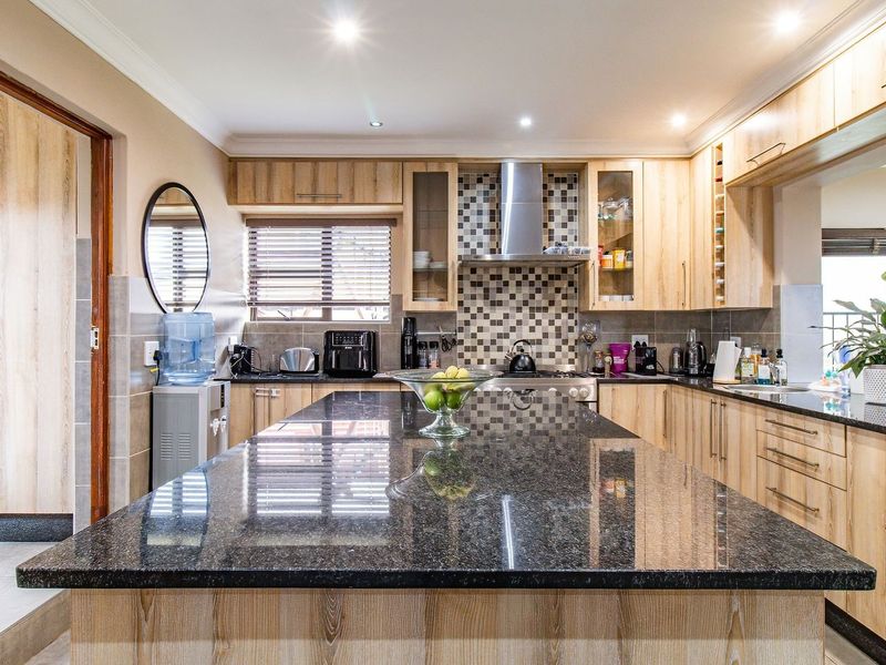 Modern kitchen featuring a large granite-topped island, light wood cabinetry, mosaic tile backsplash, and integrated stainless steel extractor fan.