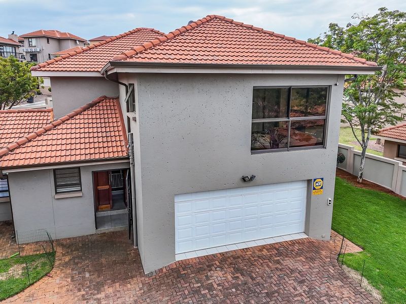 A two-story residential property featuring a tiled roof, a white sectional garage door, and a paved driveway, set within a landscaped estate environment.