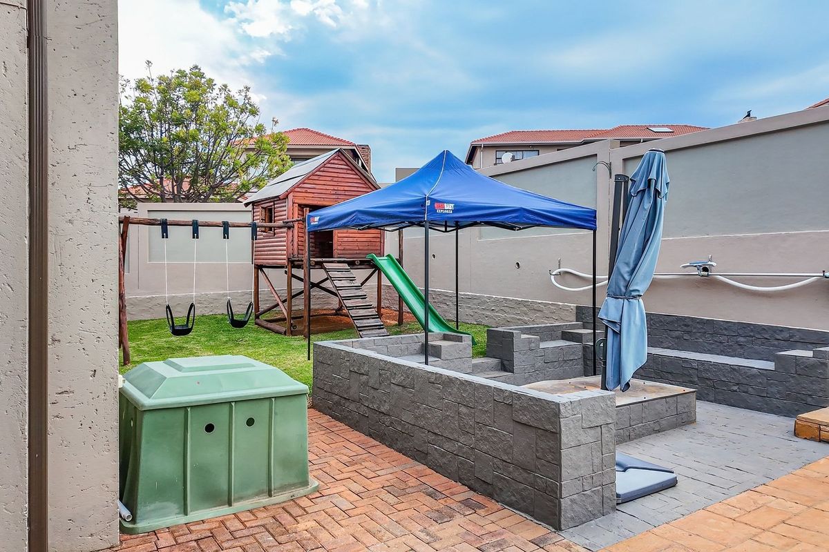A private rear garden featuring brick paving, a built-in retaining wall, and a dedicated play area with a wooden jungle gym.
