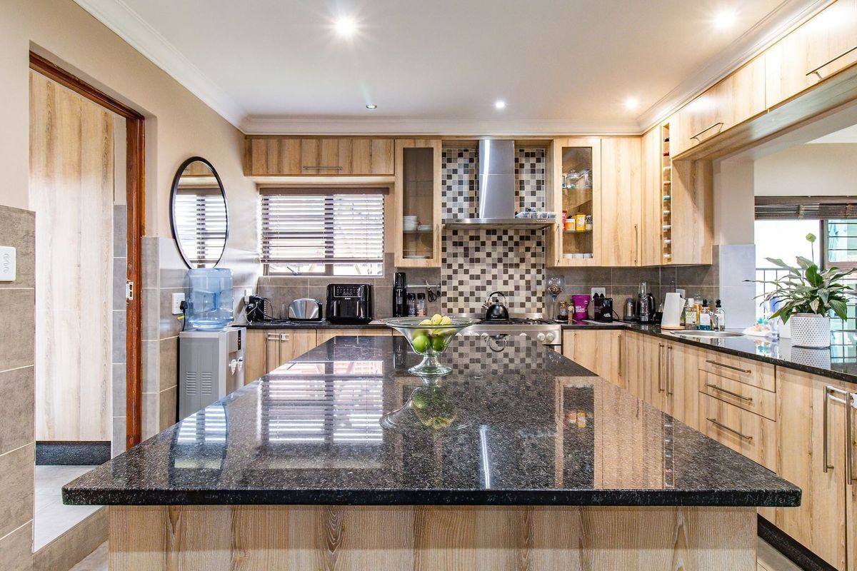Modern kitchen featuring a large granite-topped island, light wood cabinetry, mosaic tile backsplash, and integrated stainless steel extractor fan.