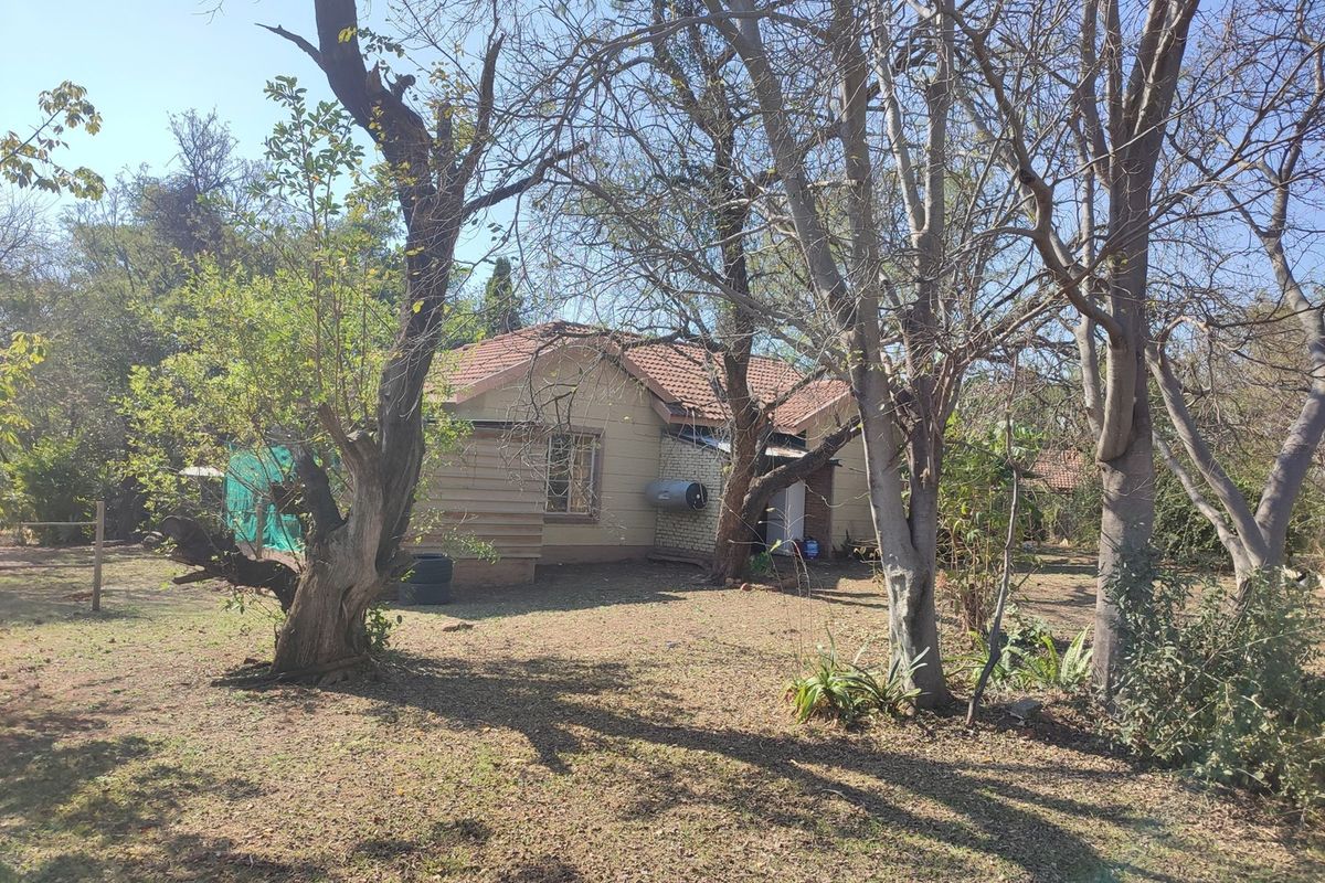 Rear view of a farm-style dwelling featuring a tiled roof and external geyser, surrounded by mature trees and natural garden space.