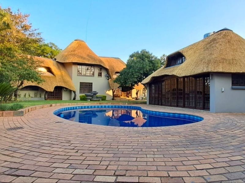 A well-maintained outdoor pool area featuring a swimming pool, paved surround, and distinctive thatched-roof architecture set within a landscaped garden.