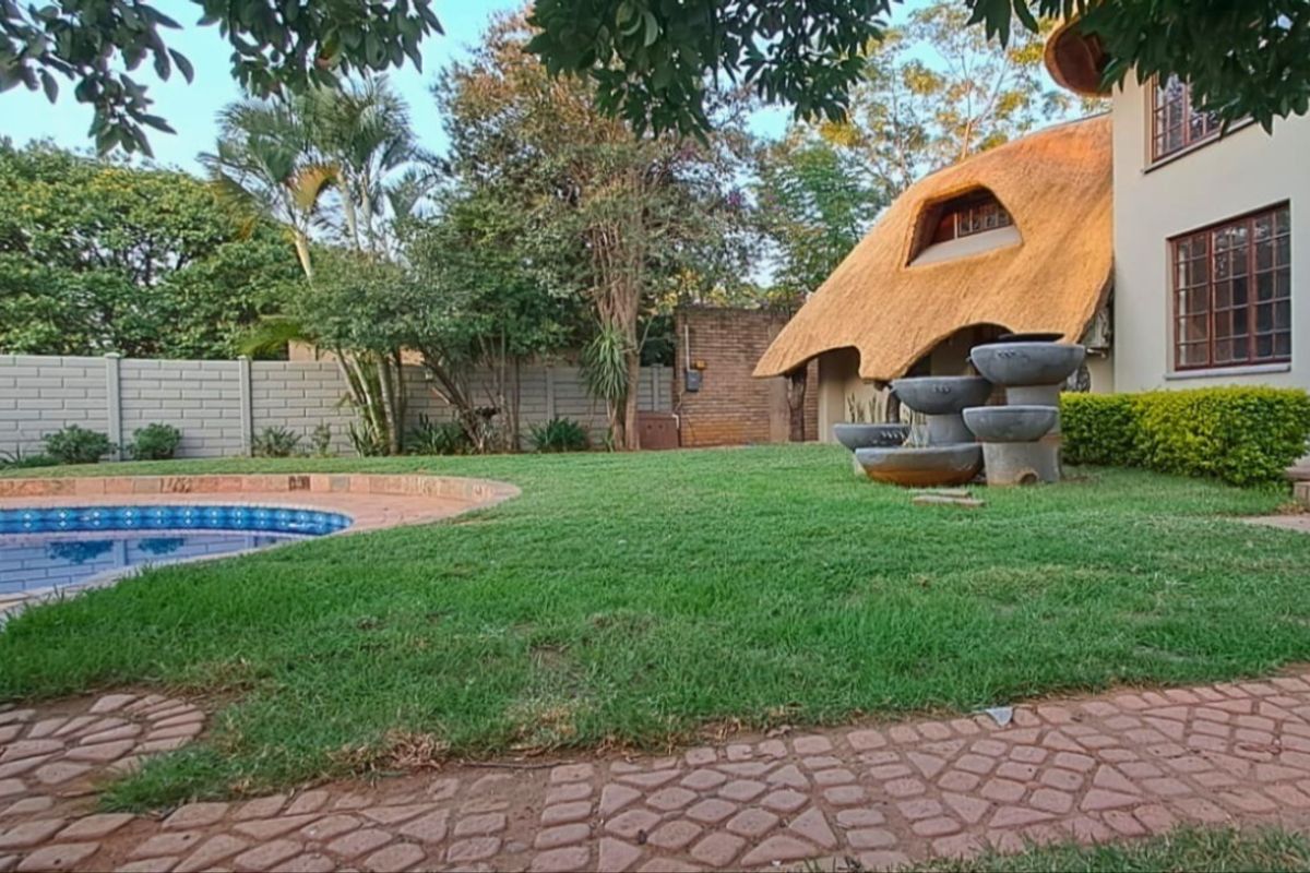 A well-maintained rear garden featuring a swimming pool, brick paving, a decorative water feature, and a distinctive thatched roof house exterior.