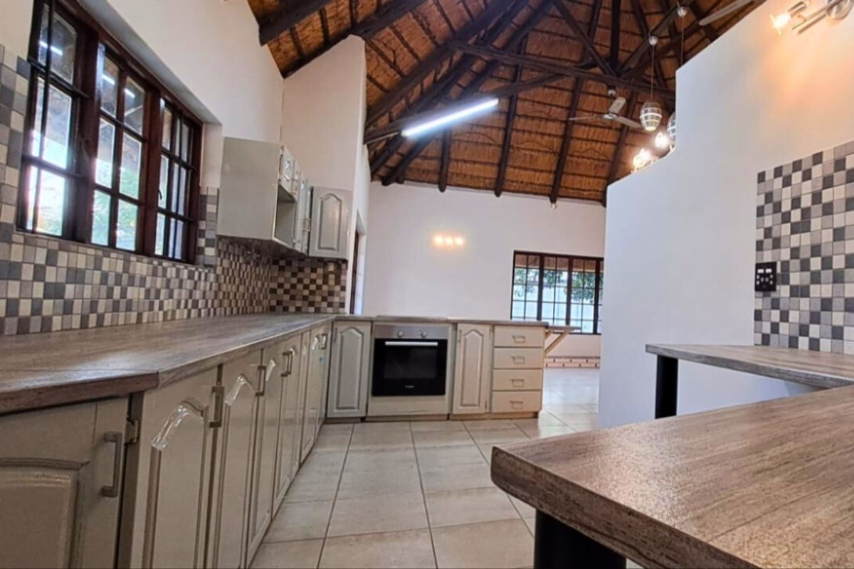 Spacious kitchen featuring a unique exposed thatch roof, tiled flooring, built-in oven, and ample laminate countertop workspace.