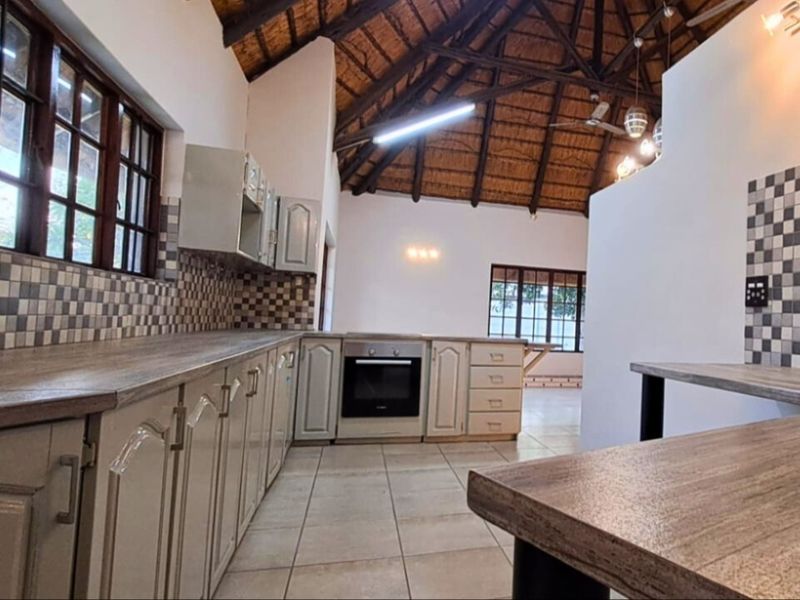 Spacious kitchen featuring a unique exposed thatch roof, tiled flooring, built-in oven, and ample laminate countertop workspace.