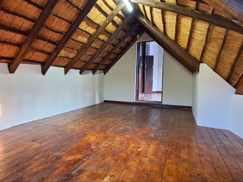 An empty attic-style bedroom featuring exposed timber rafters, a traditional thatched roof, and original timber floorboards.