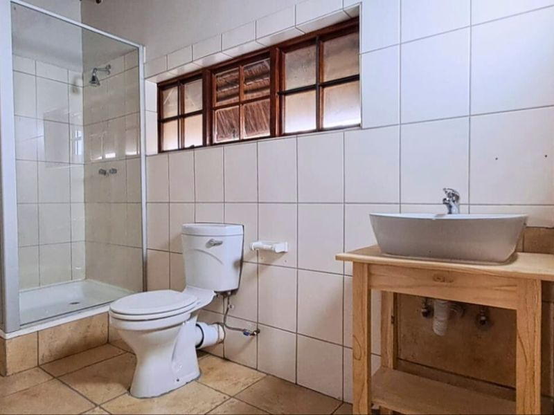 A functional bathroom featuring a glass-enclosed shower, a white toilet, and a vessel sink set on a wooden vanity with tiled finishes.