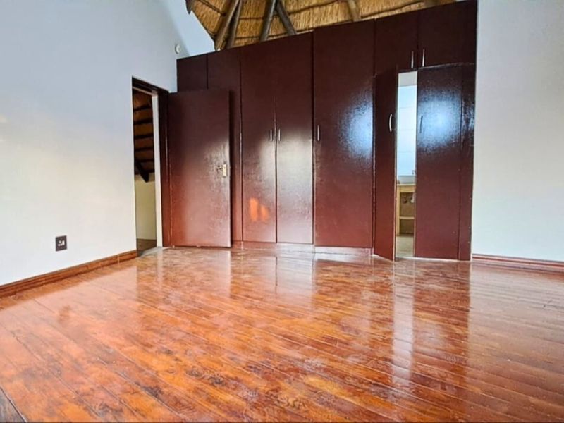 Spacious bedroom featuring polished timber flooring, built-in dark wood cupboards, and a high vaulted thatched ceiling.