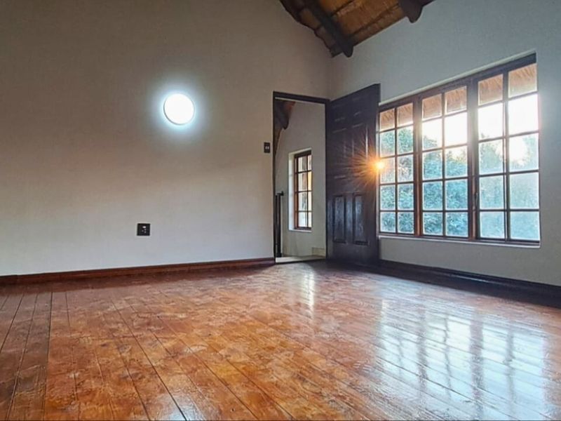 Spacious bedroom featuring polished timber flooring, exposed thatch ceiling, and large timber-framed windows allowing for natural light.