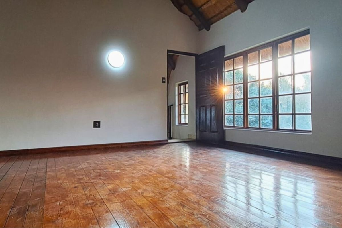Spacious bedroom featuring polished timber flooring, exposed thatch ceiling, and large timber-framed windows allowing for natural light.