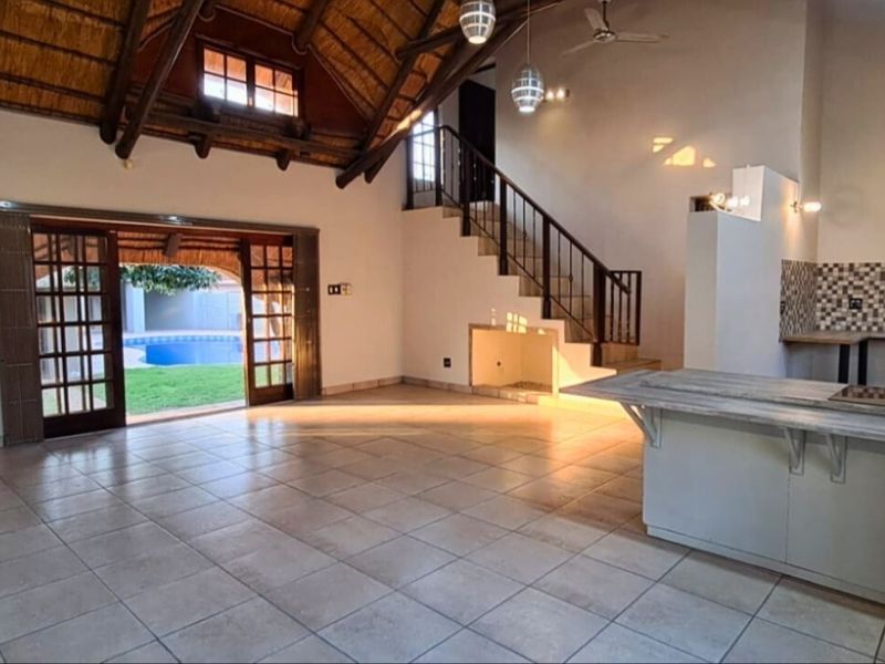 Spacious open-plan living area featuring a high thatched ceiling with exposed trusses, tiled floors, a kitchen island, and direct access to the pool area.