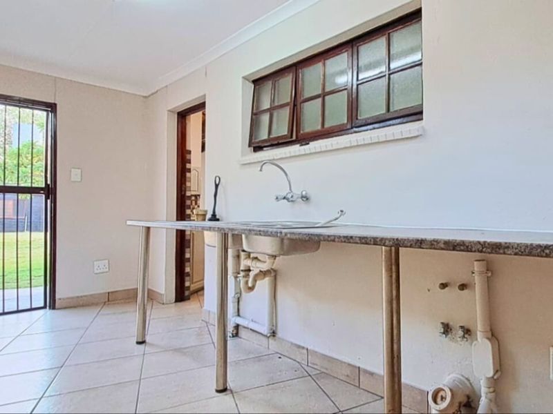A functional laundry area featuring tiled flooring, a stainless steel sink, and direct access to the rear garden through a security gate.