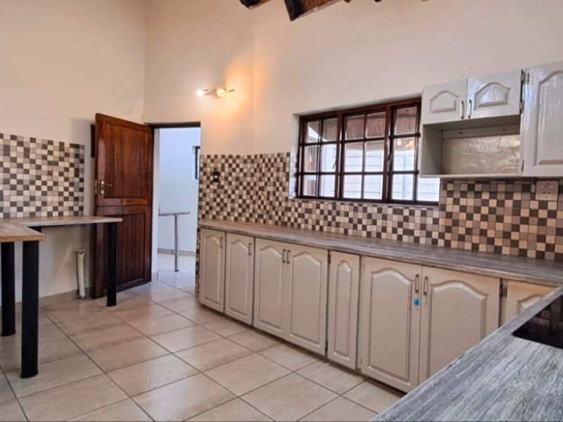 A functional kitchen featuring tiled flooring, a patterned backsplash, built-in cabinetry, and a laminate countertop with an integrated hob.