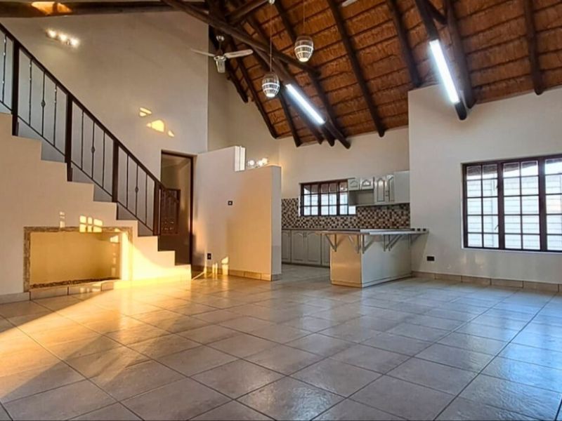 Spacious open-plan living area featuring a high thatched ceiling with exposed beams, tiled flooring, a staircase, and a functional kitchen with built-in cabinetry.