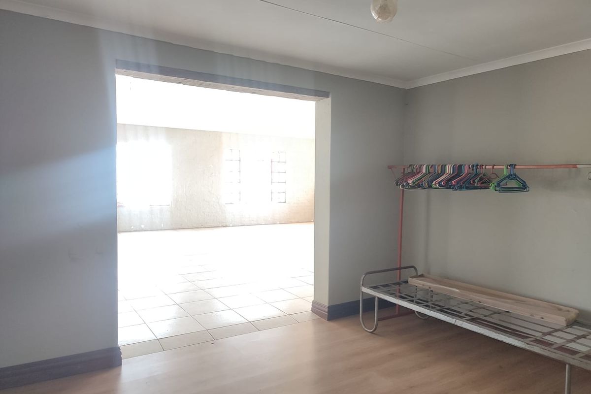 An interior view of a living area featuring laminate flooring, leading into an adjacent tiled space with natural light.