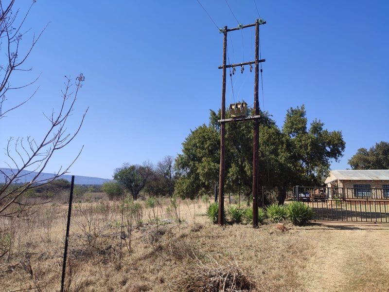 A view of the farm grounds featuring an electrical transformer on utility poles, wire fencing, and a metal gate leading to the property.