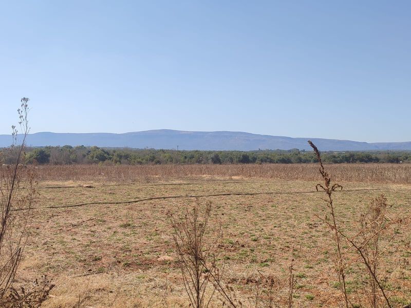 Expansive rural landscape view featuring open farmland with visible irrigation infrastructure and distant mountain ranges under a clear sky.