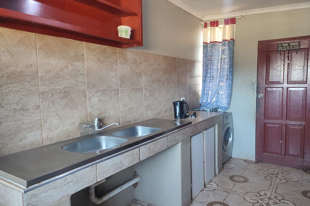 A functional kitchen area featuring a double stainless steel sink, tiled backsplash, and built-in concrete cabinetry with open shelving.