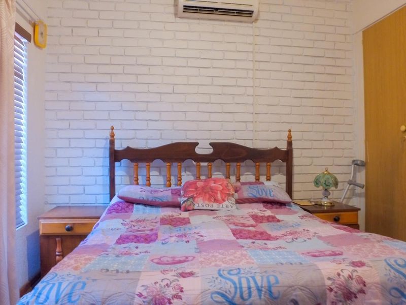 A bedroom featuring a painted brick feature wall, built-in wardrobe, and wall-mounted air conditioning unit.